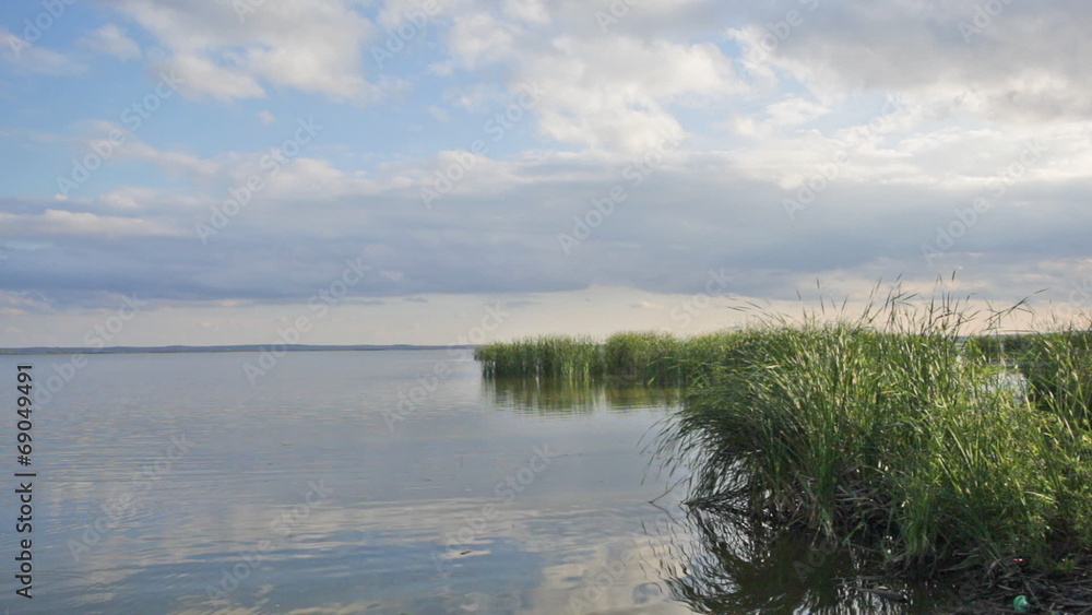 Sky with clouds and a grass are reflected in lake water Sky with clouds and a grass are reflected in lake water