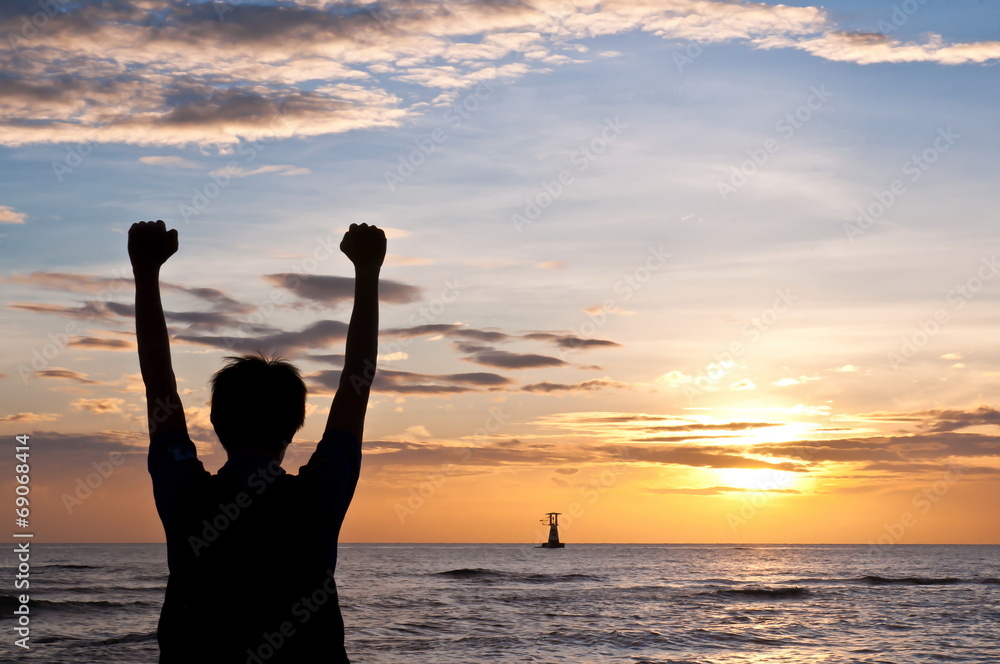 Successful man raising arms on the beach sunset