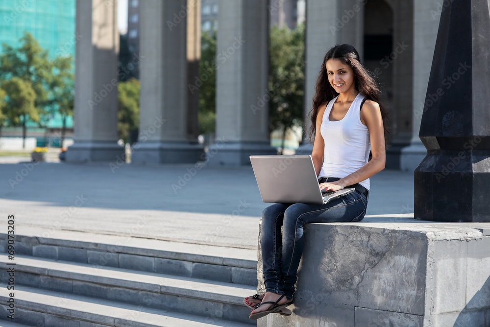 A young woman with a laptop sitting on the stairs, near the univ A young woman with a laptop sitting on the stairs, near the univ