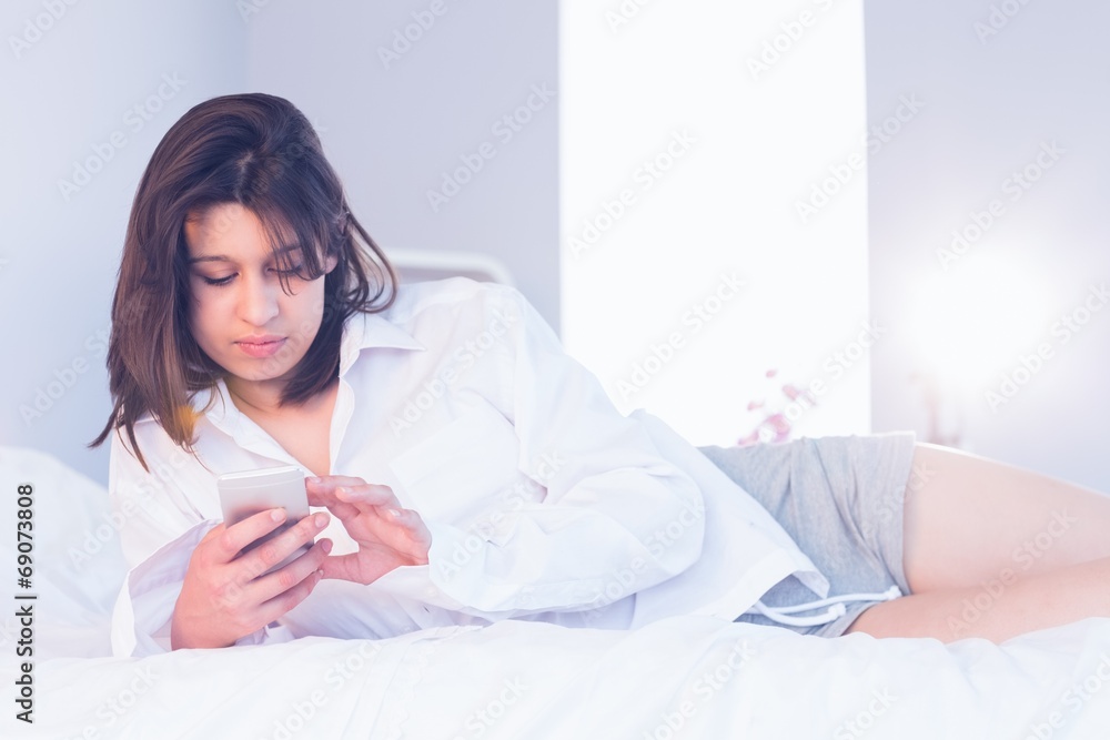 Sexy brunette sitting on her bed using smartphone