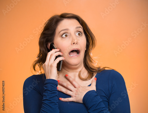 Woman receiving shocking news on phone, orange background 