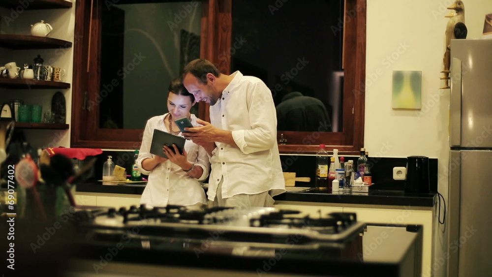 Couple with tablet and smartphone talking in kitchen Couple with tablet and smartphone talking in kitchen