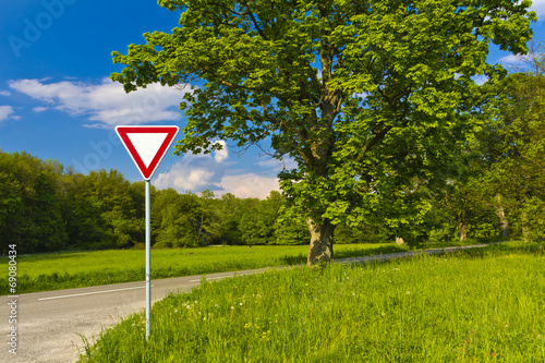 Give away fraffic sign near trees and road photo