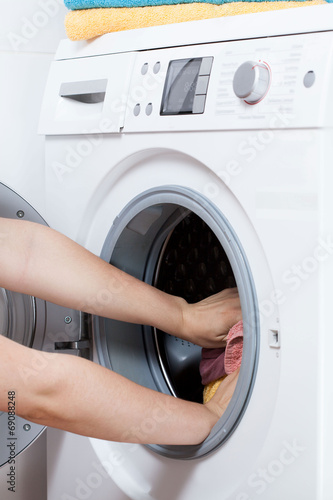 Hands putting laundry into the washing machine drum