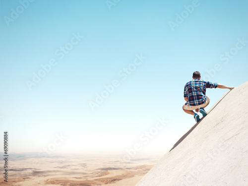 Young man sitting on a cliff and looking at the desert