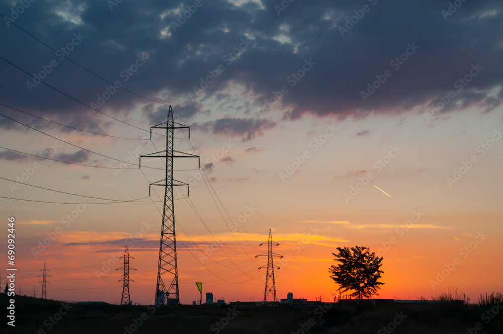 sunset over power poles, a tree and an airplane