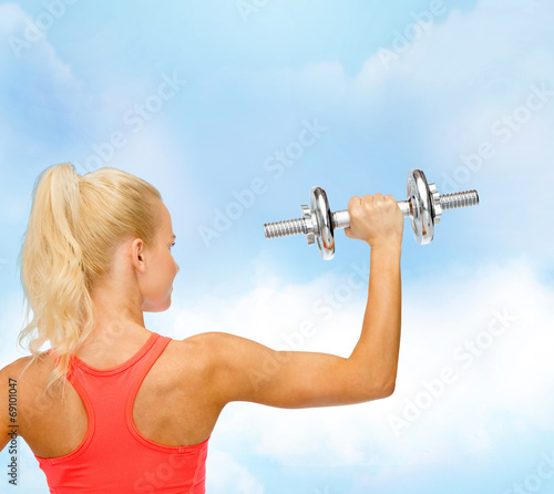 sporty woman with heavy steel dumbbell from back