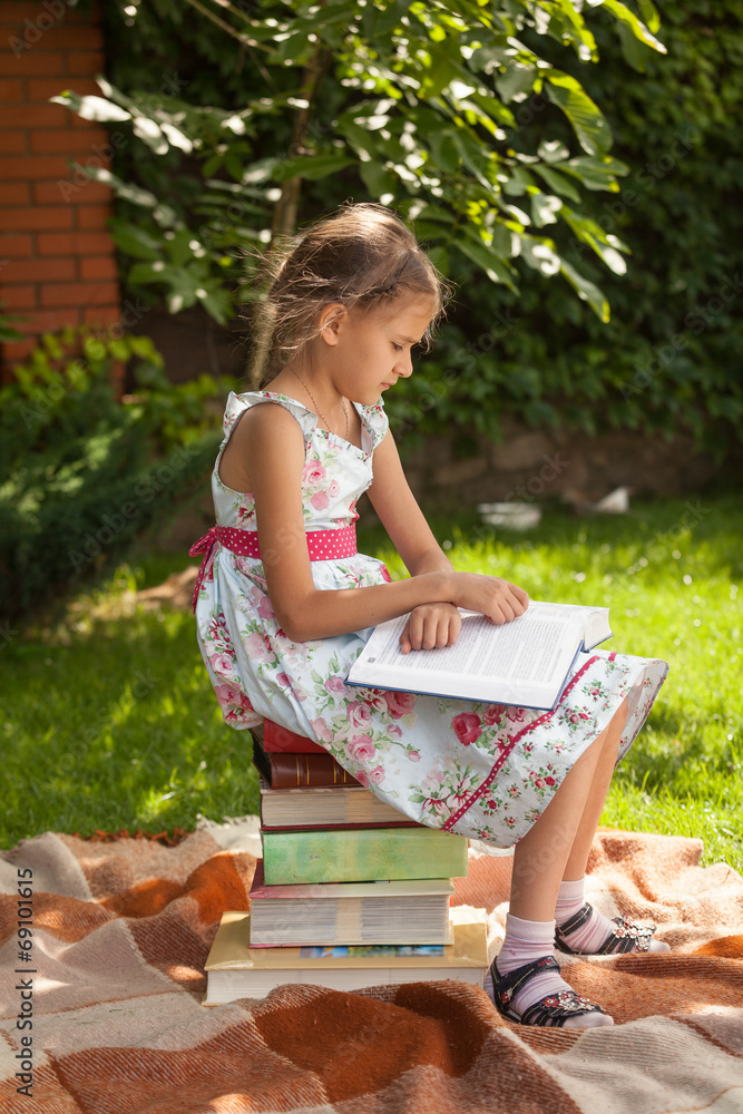 Naklejka premium smart girl reading big book at park at sunny day