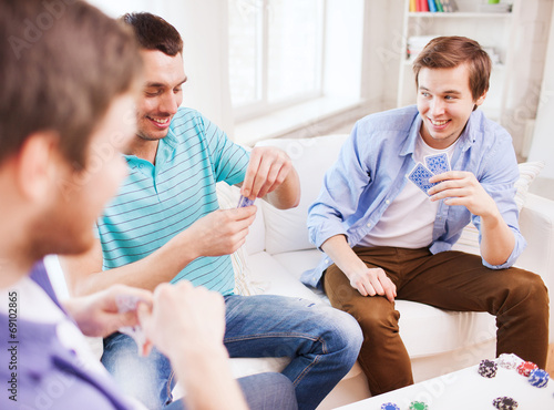 three smiling male friends playing cards at home
