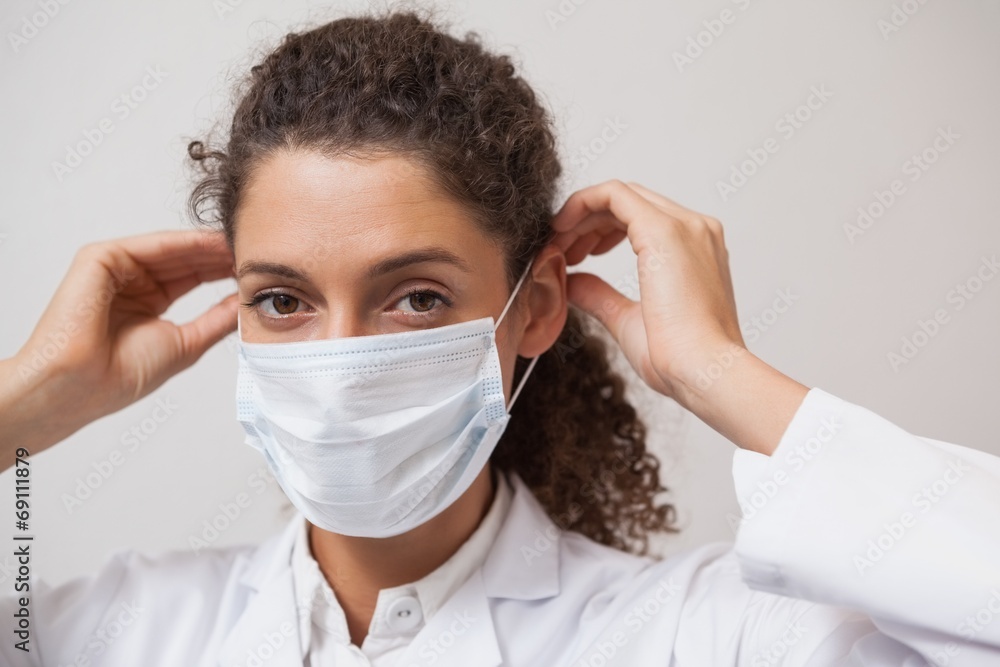 Dentist putting on surgical mask looking at camera Dentist putting on surgical mask looking at camera
