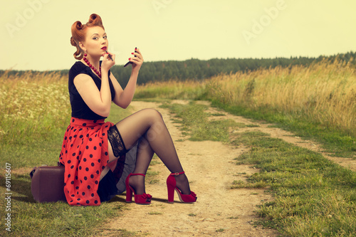woman  sitting on the side of a rural road painting lipstick. photo