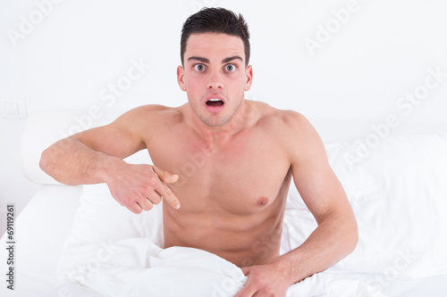 half naked young man in bed  looking down at his underwear at hi