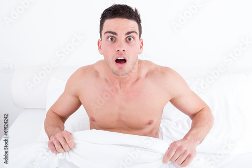 shocked half naked young man in bed  looking down at his underwe photo