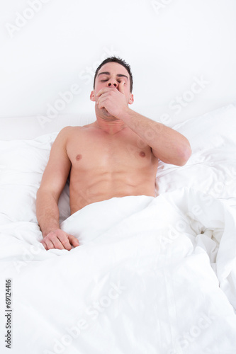 sleepy man yawning in bed at home waking up