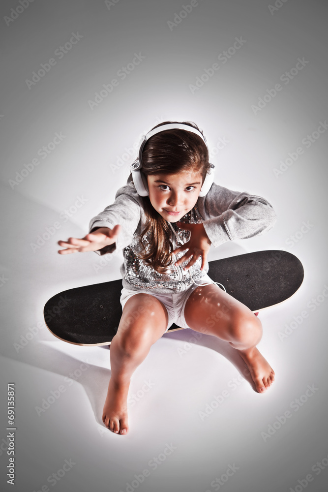 Portrait of a beautiful cool little girl sitting on a skateboard