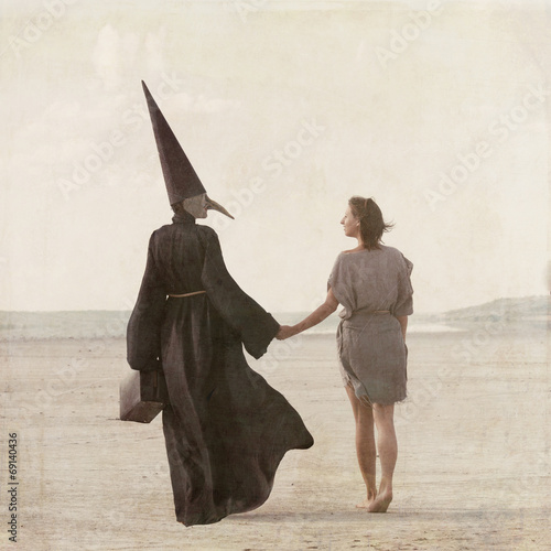 фотографія Woman and person in plague mask walking away through desert