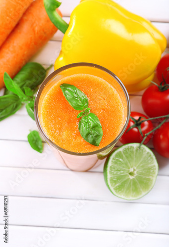 Glass of fresh carrot juice and vegetables on wooden background