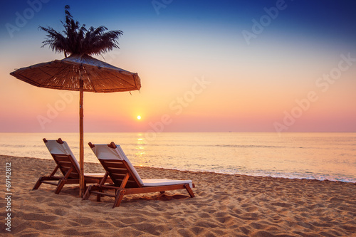 Vivid sunrise on a beautiful sandy beach with sunshade