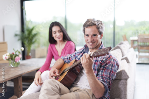 couple at home man at foreground playing guitar