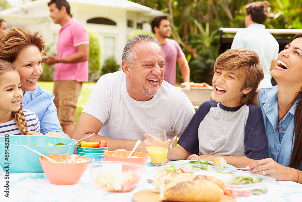 Multi Generation Family Enjoying Meal In Garden Together Multi Generation Family Enjoying Meal In Garden Together