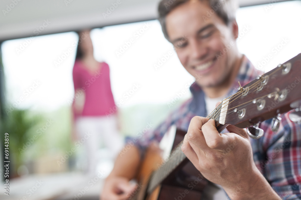 couple at home man at foreground playing guitar