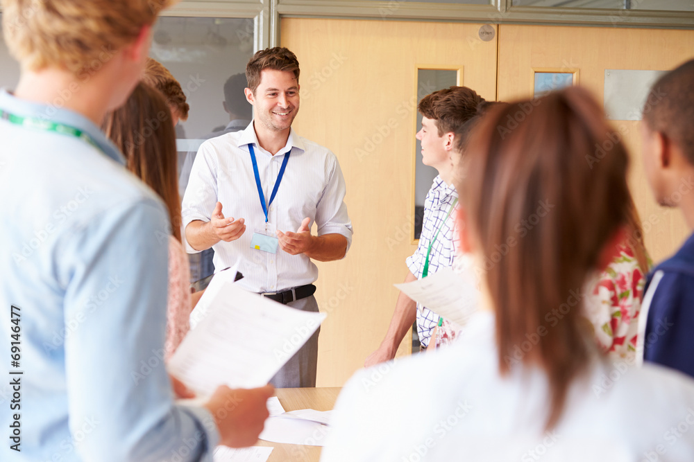Teacher With College Students Standing By Desks In Classroom Teacher With College Students Standing By Desks In Classroom