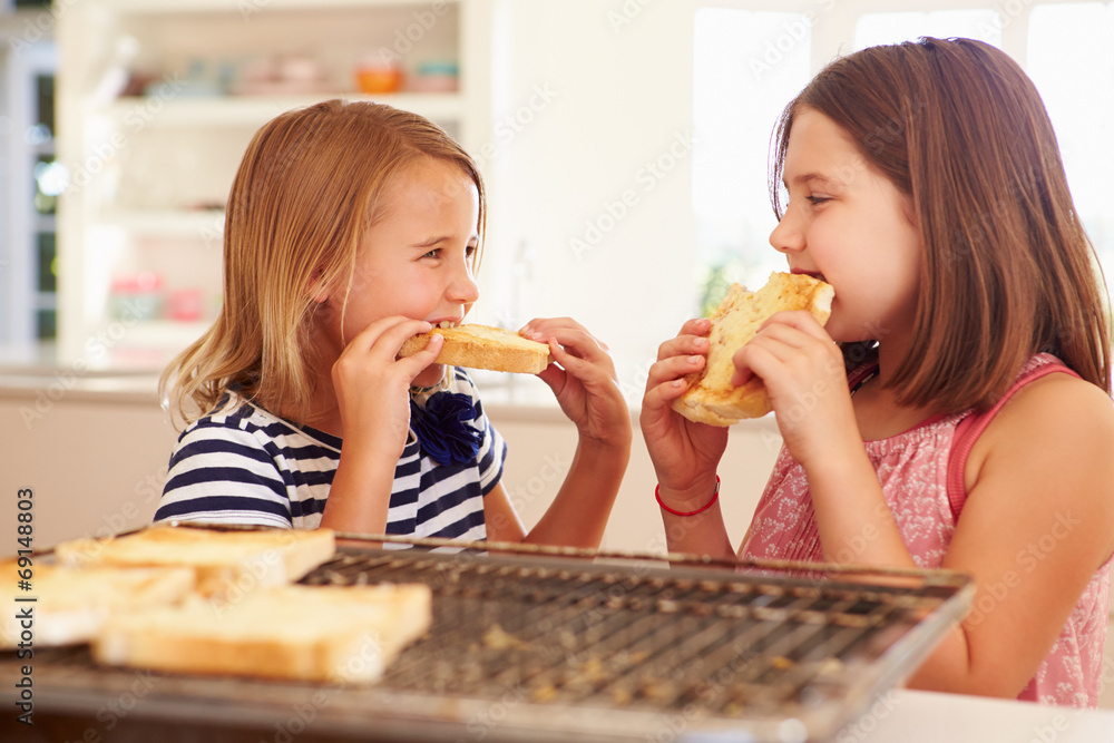 Two Girls Eating Cheese On Toast In Kitchen Two Girls Eating Cheese On Toast In Kitchen