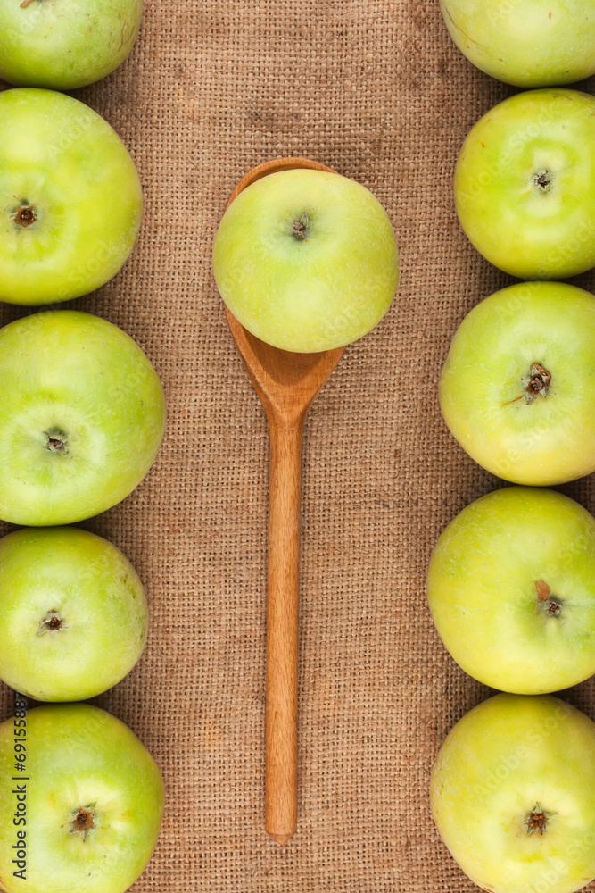 Spoon with green apple lying on the sackcloth among green apples Spoon with green apple lying on the sackcloth among green apples