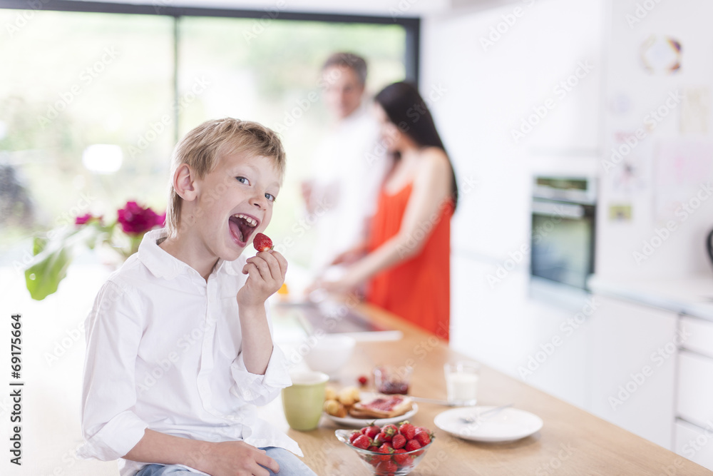 young boy eating strawberries in family kitchen young boy eating strawberries in family kitchen