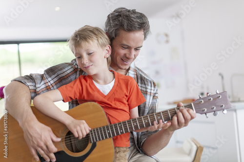 father learning his boy to play guitar