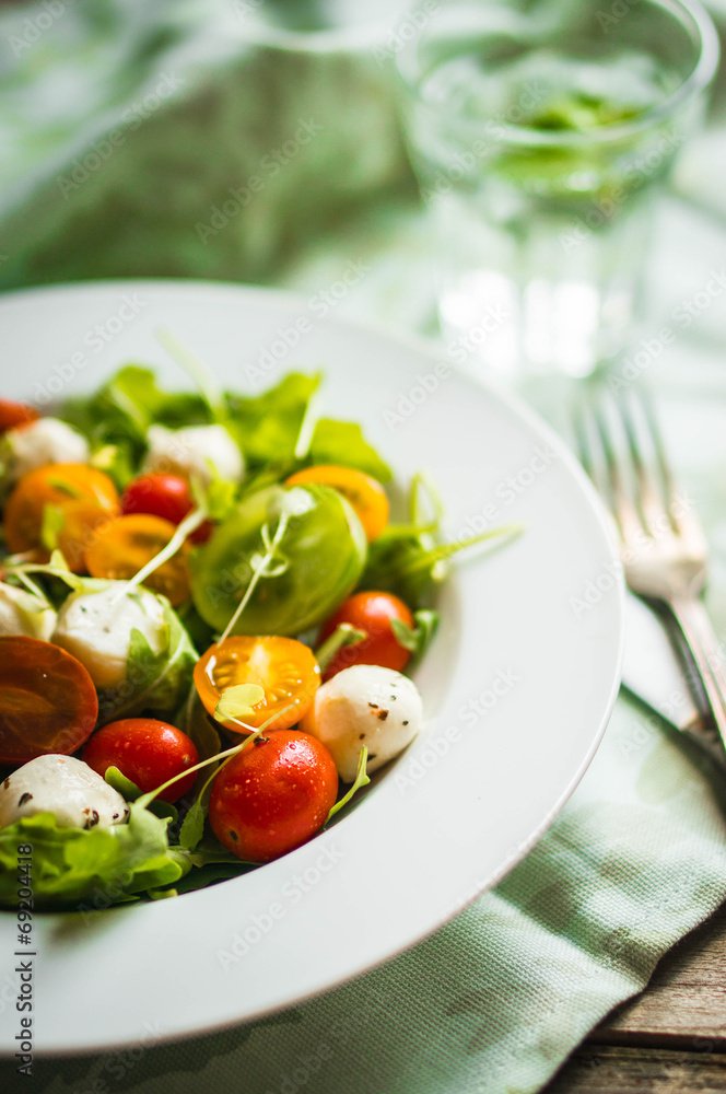 Salad with arugula,tomatoes and mozarella on wooden background Salad with arugula,tomatoes and mozarella on wooden background