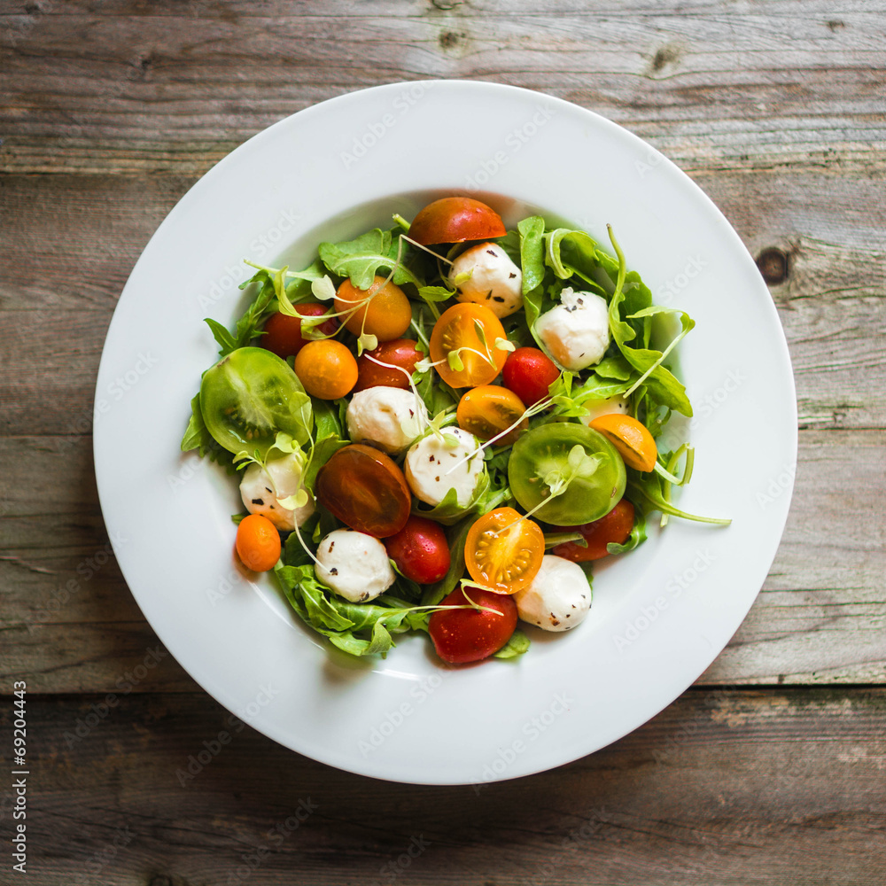 Salad with arugula,tomatoes and mozarella on wooden background Salad with arugula,tomatoes and mozarella on wooden background