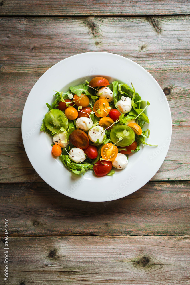Salad with arugula,tomatoes and mozarella on wooden background Salad with arugula,tomatoes and mozarella on wooden background
