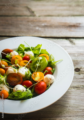 Salad with arugula,tomatoes and mozarella on wooden background