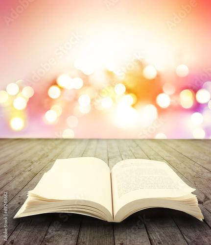 Pages of open book on table or floor in front of bright abstract background