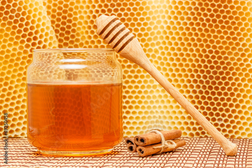Honey in jar with dipper, cinnamon and honeycomb on mat