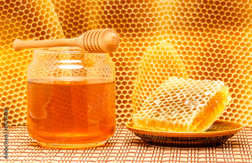 Honey in jar with dipper and honeycomb on mat