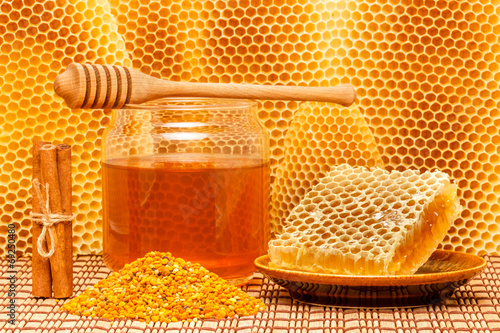 Honey in jar with dipper, honeycomb, pollen and cinnamon on mat