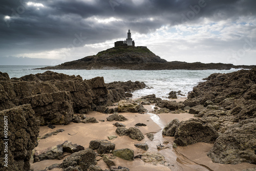 Lighthouse landscape with stormy sky over sea with rocks in fore photo