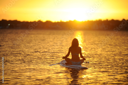 Frau  meditiert auf Surfboard im See