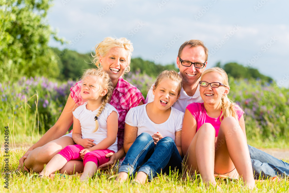 Familie sitzt im Grass auf Feld oder Wiese