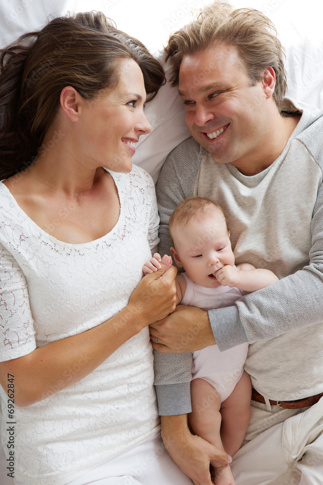 Smiling man and woman hugging baby in bed