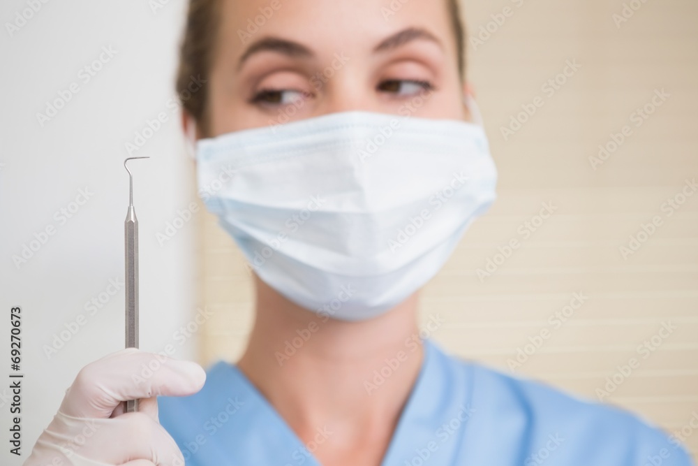 Dentist in surgical mask holding dental explorer Dentist in surgical mask holding dental explorer