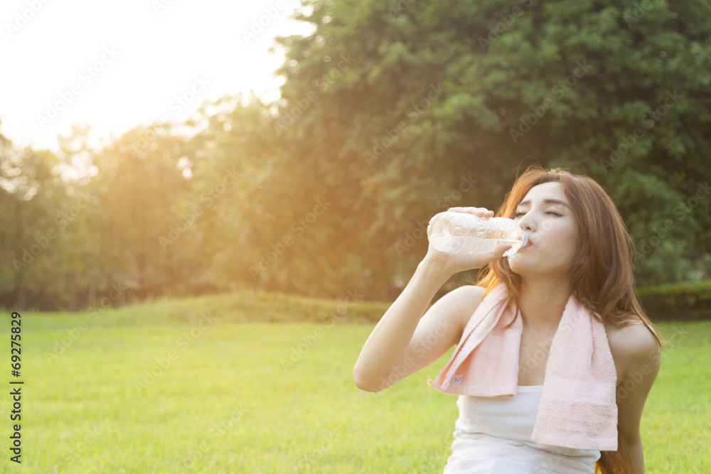 Woman drinking water and sit on grass. - obrazy, fototapety, plakaty 