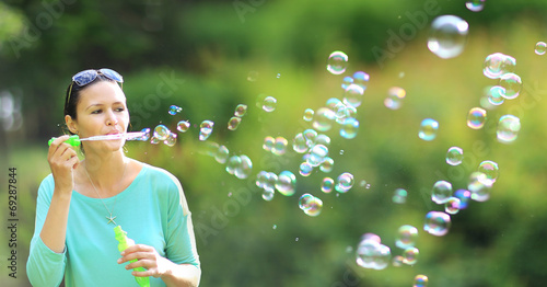 Canvas-taulu brunette girl blowing soap bubbles in sunlit park.