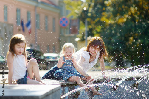 Konstfotografi Young woman and two kids by a city fountain