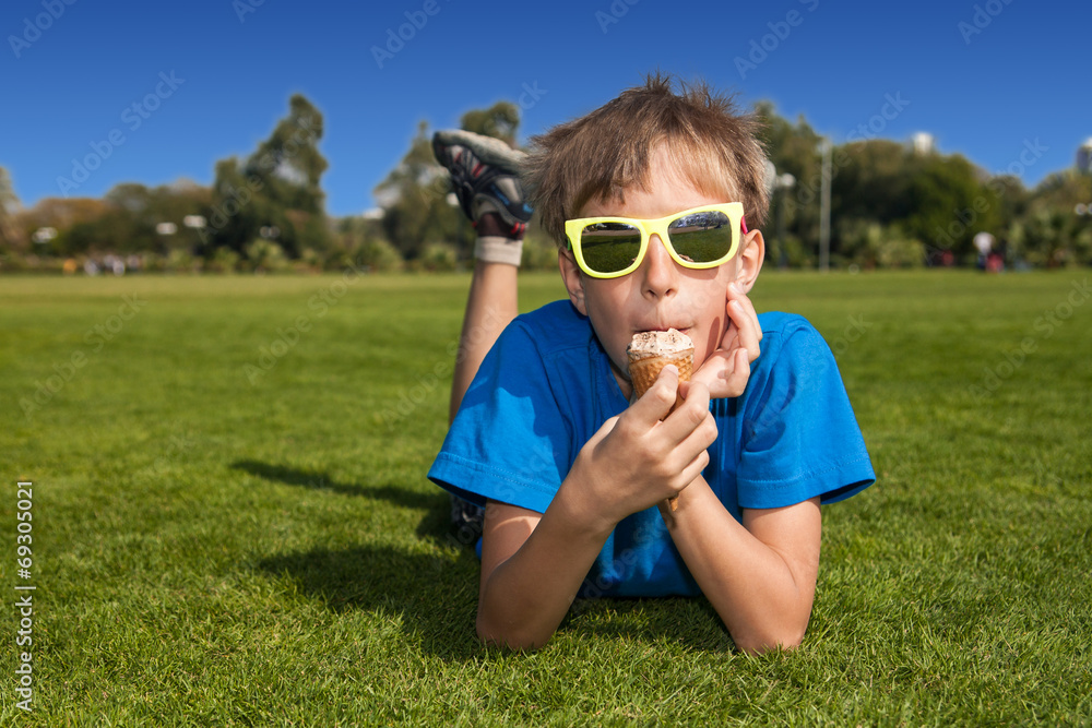 Funny boy with sunglasses lying on grass eating ice-cream Funny boy with sunglasses lying on grass eating ice-cream