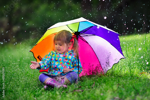 Funny cute toddler girl wearing raincoat with colorful umbrella
