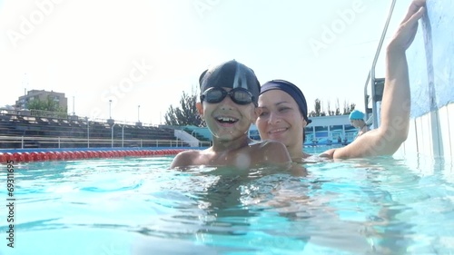 Happy pretty woman with her son in swimming pool looking happy
