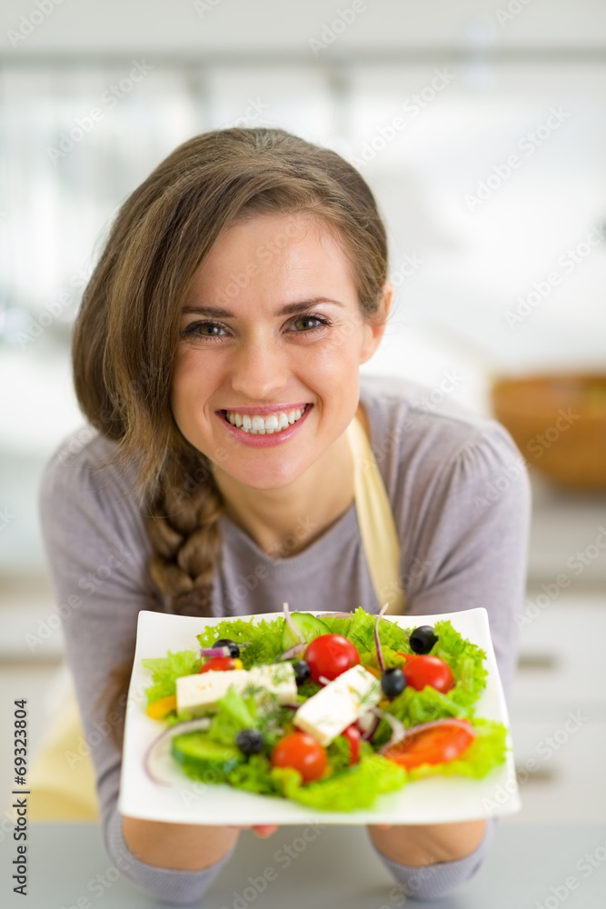 Portrait of smiling young housewife showing greek salad Portrait of smiling young housewife showing greek salad